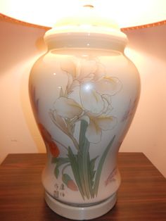 a white vase sitting on top of a wooden table next to a lampshade