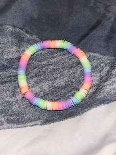 a multicolored beaded bracelet sitting on top of a gray cloth covered blanket