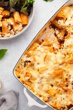 a casserole dish with meat and cheese in it next to a bowl of salad