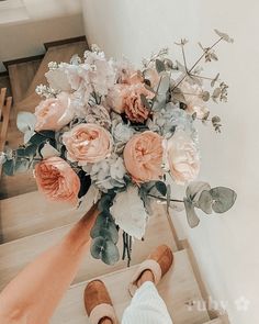 a bouquet of flowers is being held up by someone's feet on the stairs