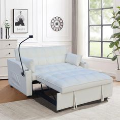 a living room with white furniture and a plant in the corner on the rugs