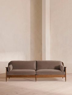 a gray couch sitting in front of a tall white wall next to a wooden floor