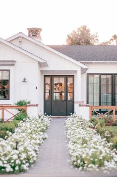 a white house with flowers in front of it and a walkway leading to the front door