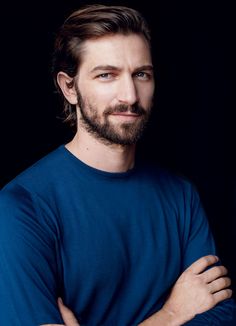 a bearded man with his arms crossed posing for a photo in front of a black background