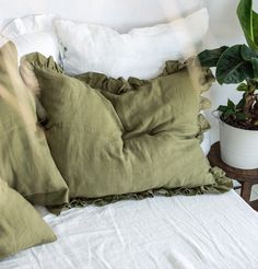 a bed topped with lots of pillows next to a potted plant