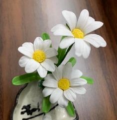 three white flowers in a small vase on a wooden table with black and white designs