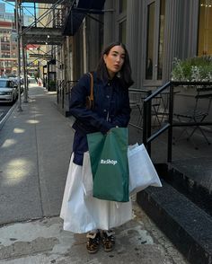 a woman is standing on the sidewalk with shopping bags