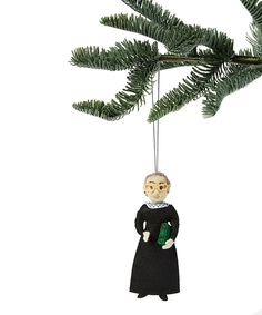 an ornament hanging from a tree with a woman wearing a black dress and holding a green book