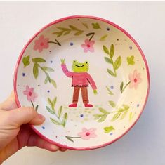 a hand holding a small bowl with an image of a frog on it