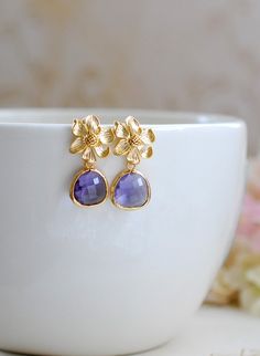 Stunning amethyst purple glass jewels and gold flowers post earrings. Sparkly glass jewels are faceted and gold framed. Flowers are matte gold plated over brass with sterling silver ear posts that are great for sensitive skin. These earrings are perfect for a romantic night out or a gold and purple themed wedding.Arrives in gift box.Measurement & Details:Total length: approx. 1.2" (29mm)Purple jewels: 13mm x 15mmEar wires: 925 sterling silver post, hypoallergenic.For more beautiful modern ea Purple Drop Earrings, Purple Wedding Theme, Gold Filigree Earrings, Vintage Style Jewellery, Gold Earrings Designs, Amethyst Purple, Gold Flower, Purple Glass, Purple Crystals