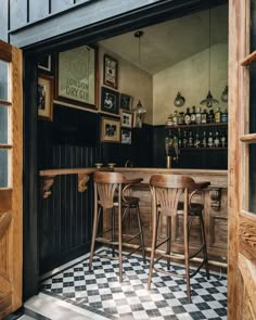 an open door leading into a bar with three stools and a checkered floor