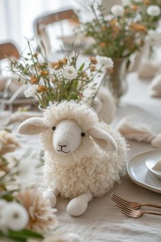 a stuffed sheep sitting on top of a table next to plates and silver utensils