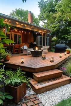 A cozy wooden deck with wicker chairs, a fire pit, string lights, and lanterns, surrounded by lush greenery and a brick patio with potted plants. Stone Patio Off Of Deck Ideas, Decks On Sloped Backyards, Wood Deck And Stone Patio, Backyard Deck Lighting, Ground Level Deck Ideas With Pergola, Ranch Home Deck Ideas, Non Wood Deck Ideas, Backyard Deck And Pergola Ideas, Long Back Deck Ideas