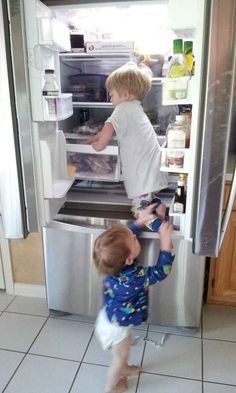 two young boys are looking into an open refrigerator and trying to get something in it