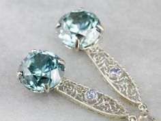 "Handcrafted in our New Hampshire studio, these earrings represent both something old, and something blue! The drops have been converted from an early 1900's era bar pin, set with light blue sapphires, and the filigree provides a pretty cobweb motif and gives length to the sparkling blue zircon gemstones we've set below. Metal: 14K White and Yellow Gold Gem: 2 Blue Zircon totaling 17.28 Carats Gem Measurements: 11 mm, Round Accents: 2 Sapphire totaling .14 Carats Earrings Length: 47 mm Earrings Heirloom Wedding Earrings Pierced, Blue Art Deco Wedding Earrings, Heirloom Gemstone Earrings For Wedding, Heirloom Sterling Silver Earrings For Wedding, Heirloom Sterling Silver Wedding Earrings, Silver Heirloom Earrings For Formal Occasions, Sterling Silver Heirloom Earrings For Anniversary, Art Deco Gemstone Earrings For Gift, Heirloom Sterling Silver Earrings For Anniversary