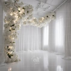 a room with white flowers and lights on the wall, along with sheer drapes