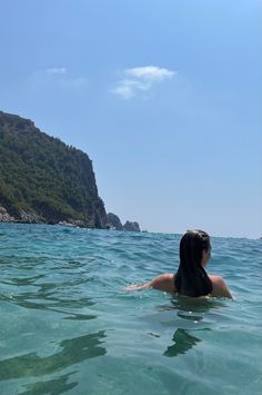 a woman swimming in the ocean near a mountain