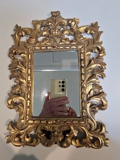 a person holding a cell phone in front of a gold framed mirror on a wall