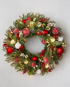 a christmas wreath with ornaments and greenery hanging on the wall in front of it