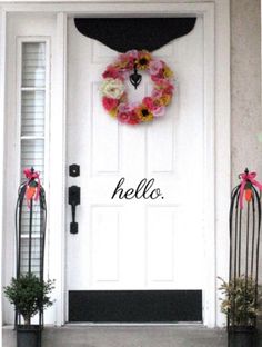 a white door with a wreath on it and some black planters in front of it