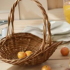 a wicker basket filled with oranges on top of a wooden table next to glasses