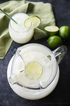 two glasses filled with white liquid and limes next to each other on a table