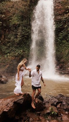 a man and woman standing in front of a waterfall