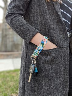 a woman wearing a gray coat and holding a keychain with flowers on it