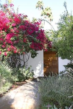 an open door in the middle of a garden with pink flowers on it's side