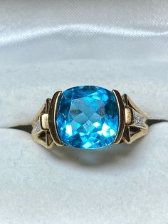 Love blue? This 10K yellow gold ring features a checkerboard faceted cushion cut blue topaz as the star. It measures 10mm x 10mm and secured in a semi bezel mounting. That makes it a 3.5 carat stone. The checkerboard faceting makes it dazzle! Flanking the center stone is are 2 diamond chips in an illusion setting. The ring is a size 8 and weighs in at 4.6 grams. It is a gorgeous ring for any occasion! Swirl Diamond Ring, White Gold Diamond Rings, Love Blue, Yellow Gold Ring, Gold Diamond Rings, Topaz Ring, Diamond Sizes, Cushion Cut, Yellow Gold Rings