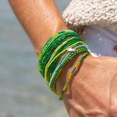 a close up of a person's arm with bracelets on their wrists and the ocean in the background