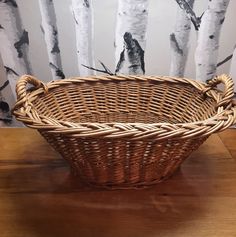 a wicker basket sitting on top of a wooden table in front of birch trees