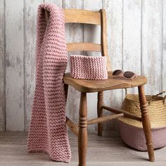 a pink knitted blanket sitting on top of a wooden chair next to a basket