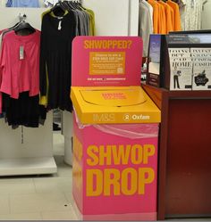 a store display with clothes and t - shirts for sale in the background, including a pink box that says shwop drop