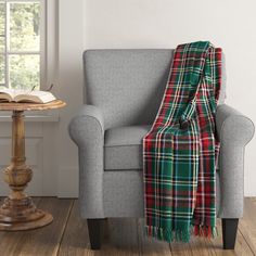 a chair with a plaid blanket on it next to a book and a small table