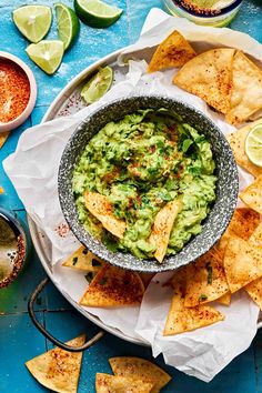 a bowl filled with guacamole surrounded by tortilla chips and lime wedges