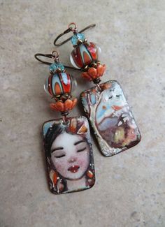 two earrings with an image of a woman hanging from the earwires on a marble surface