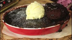 a chocolate cake with ice cream in a red dish on top of a wooden table