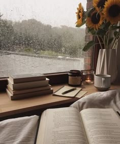 an open book sitting on top of a window sill next to a vase filled with sunflowers