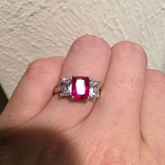 a woman's hand holding a ring with three stones on it and the center stone is red