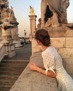 a woman sitting on top of a stone wall next to statues