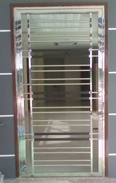 an open glass door with metal bars on the outside and inside, in front of a gray wall