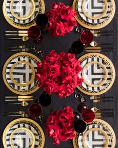 the table is set with red roses and black plates, gold rimmed cutlery