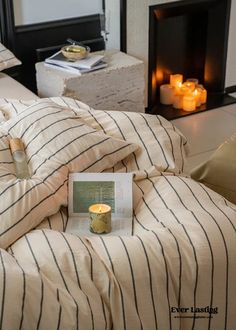 a book on a bed next to a fireplace with lit candles in the room behind it