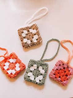 three crocheted square ornaments are sitting on a white surface and one is hanging from a string