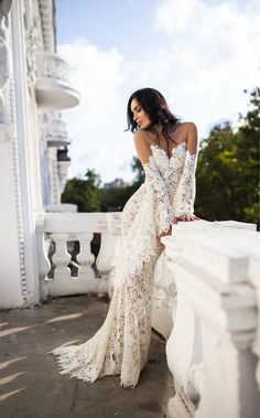 a woman in a long white dress leaning on a wall with her back to the camera