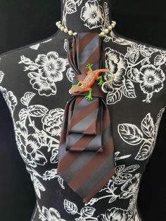 This  Chocolate Brown Striped Necktie Necklace is made with a (Barry Wang) woven silk tie, and features a Multi-Color Rhinestone Brooch strung on your choice of an adjustable Rosary Chain Ribbon Tie Pearl Necklace or an adjustable Elastic Band. The soft, comfortable fabric sits perfectly on any size chest, while the adjustable necklace feature allows you to customize the fit to your liking. Measuring at a versatile length, this necktie necklace is designed to be a one-size-fits-all. View all Wom Necktie Necklace, Tie Brooch, Tie Crafts, Tie Necklace, Jewelry Brooch, Women Ties, Neck Bow, Women's Tie, Handmade Beaded Necklaces