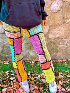 a person wearing colorful crocheted leggings standing in front of a stone wall