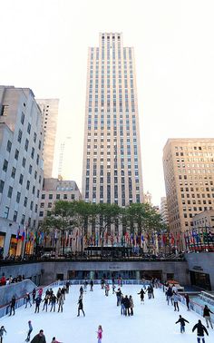 people skating on an ice rink in the middle of a large city with tall buildings