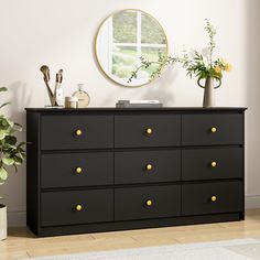 a black dresser with yellow knobs in front of a mirror and potted plant